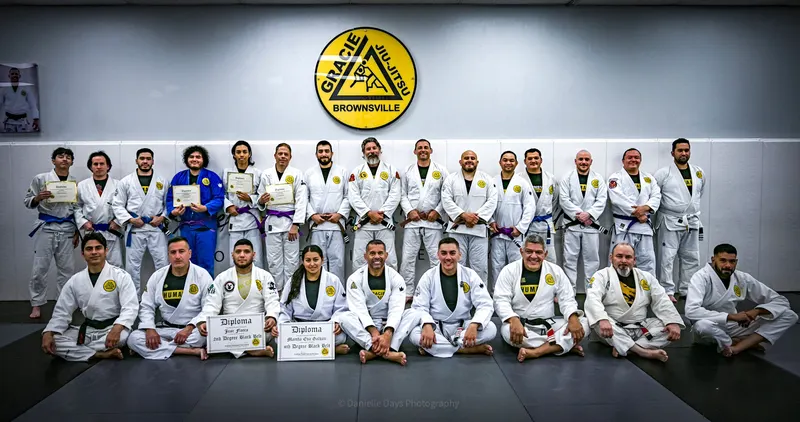 The Gracie Humaita Brownsville team in white and blue gis, lined up on the mat under the Gracie Jiu-Jitsu Brownsville crest, several holding diplomas
