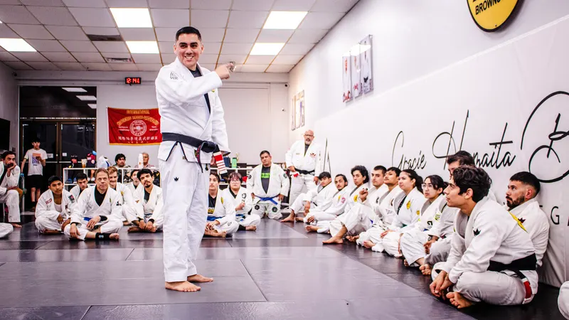 A black belt instructor speaks to a large class of students seated around the edge of the mat at Gracie Humaita Brownsville